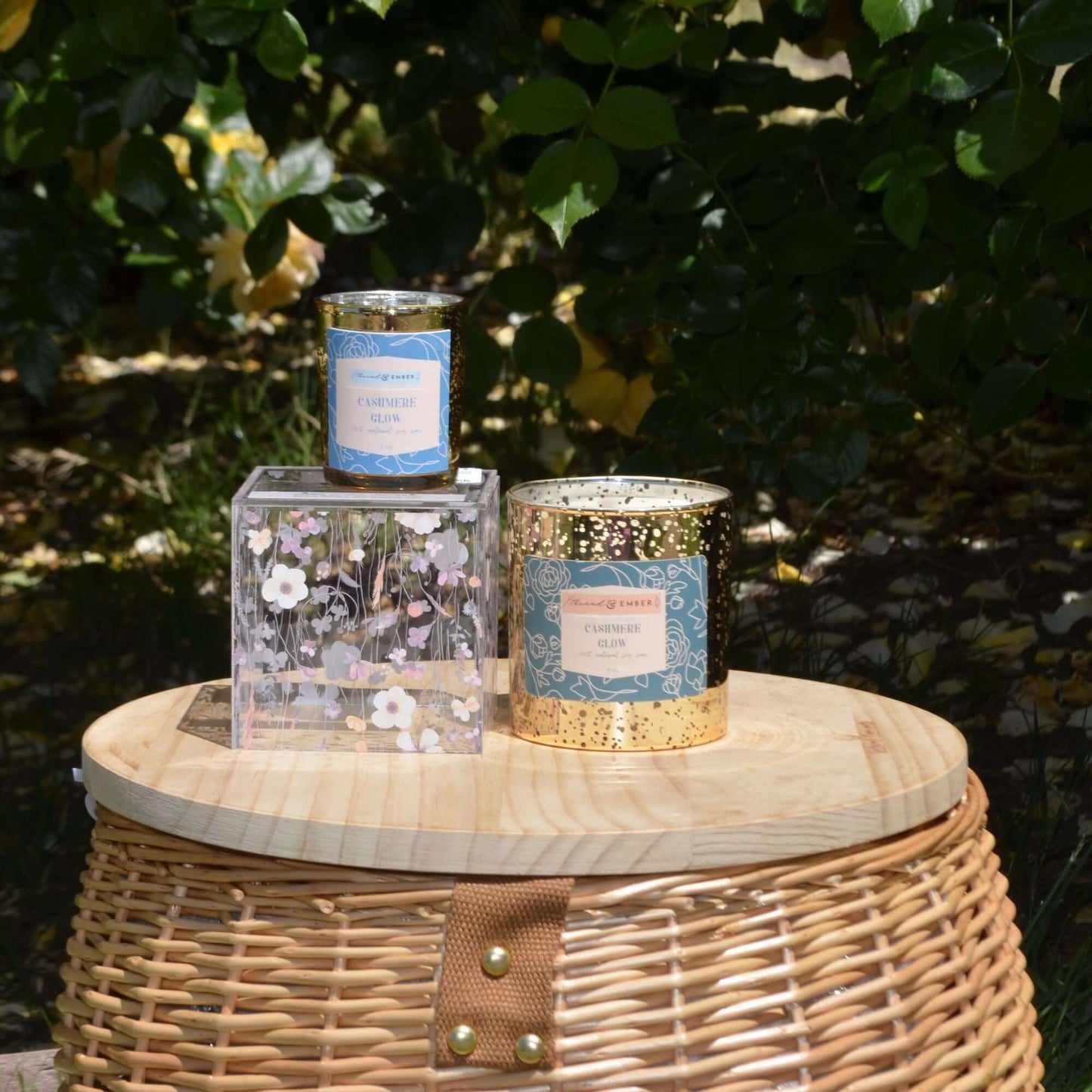 Thread & Ember Cashmere Glow candles on a wicker basket with floral background.