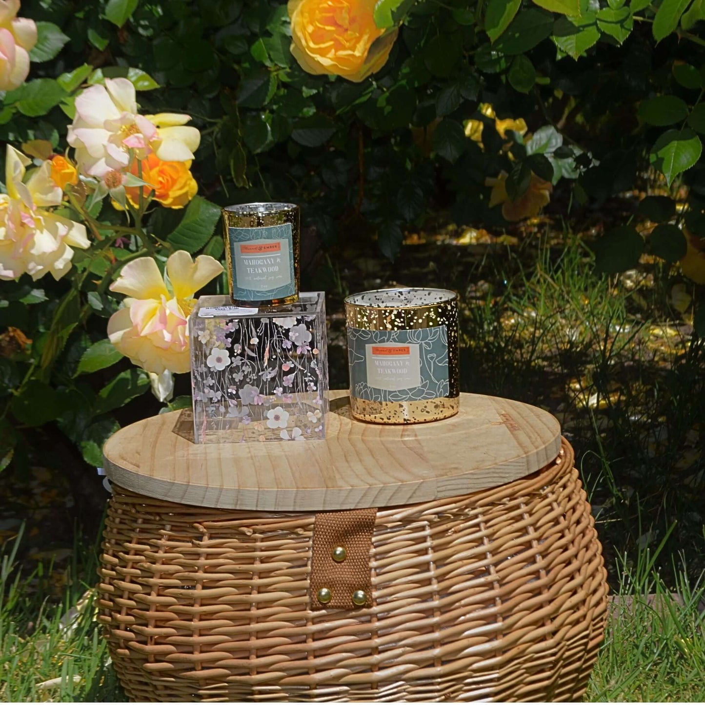 Mahogany & Teakwood Candle displayed outdoors with golden roses in the background.