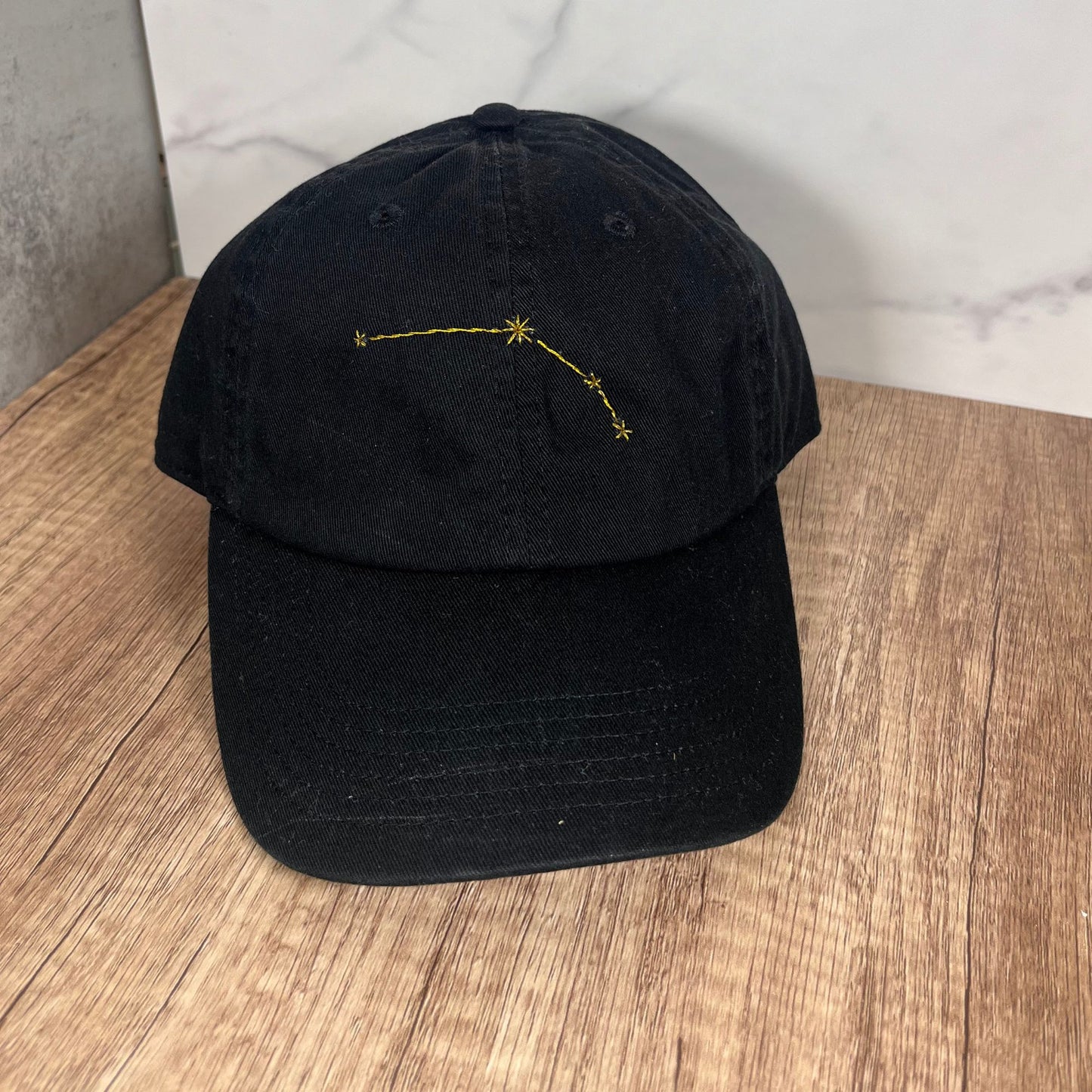 Black Aries hand-embroidered constellation baseball cap displayed on a wooden surface.
