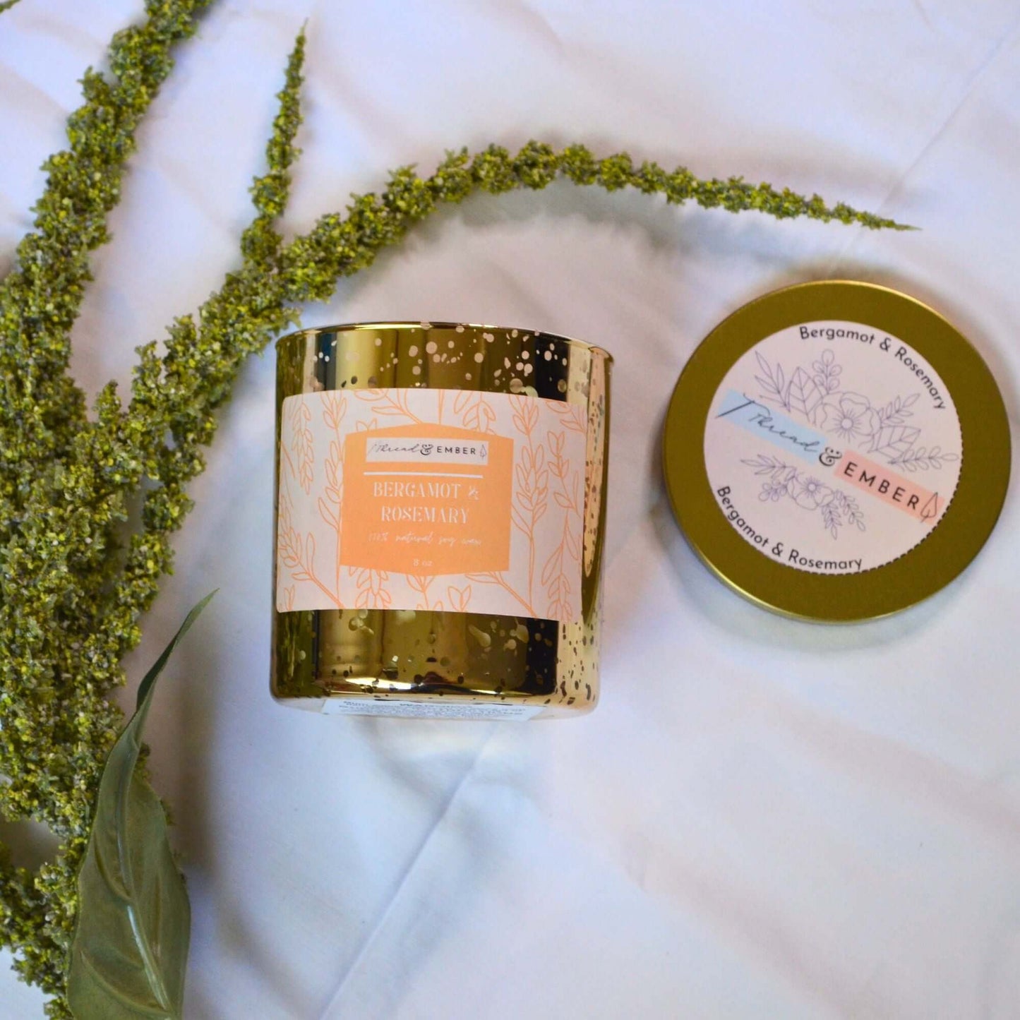 Thread & Ember Bergamot & Rosemary candle, showing its intricate label and separate lid on a white fabric background.