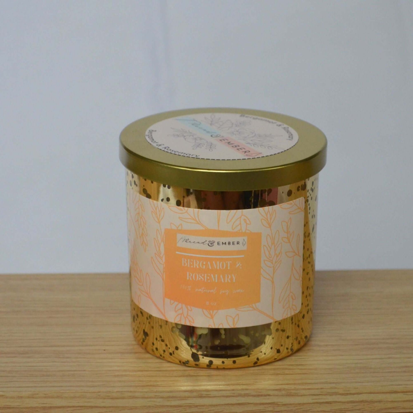 Bergamot & Rosemary candle in an 8 oz size with a golden lid, elegantly displayed on a wooden surface.