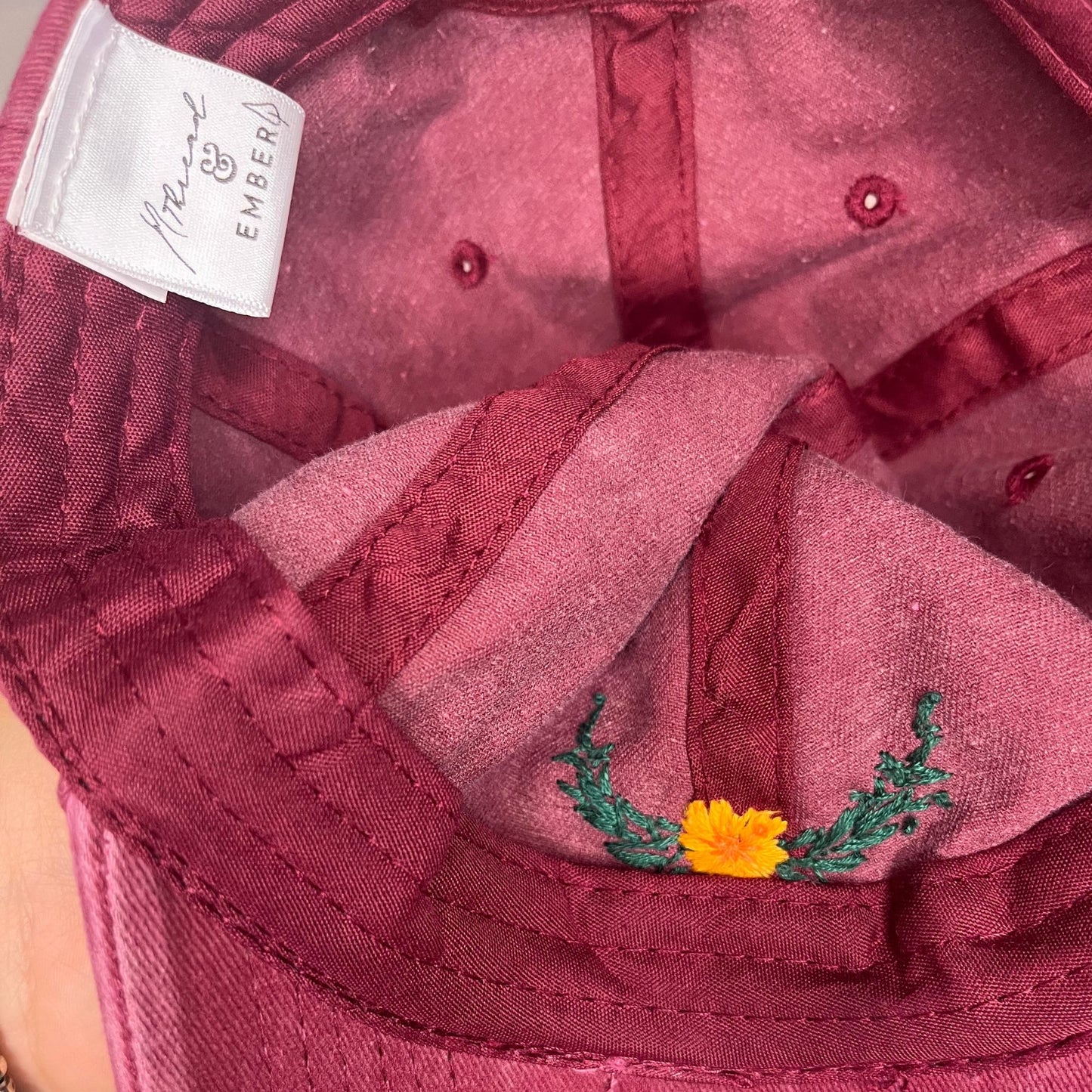 Inside view of burgundy baseball hat with floral laurel embroidery and branded label.