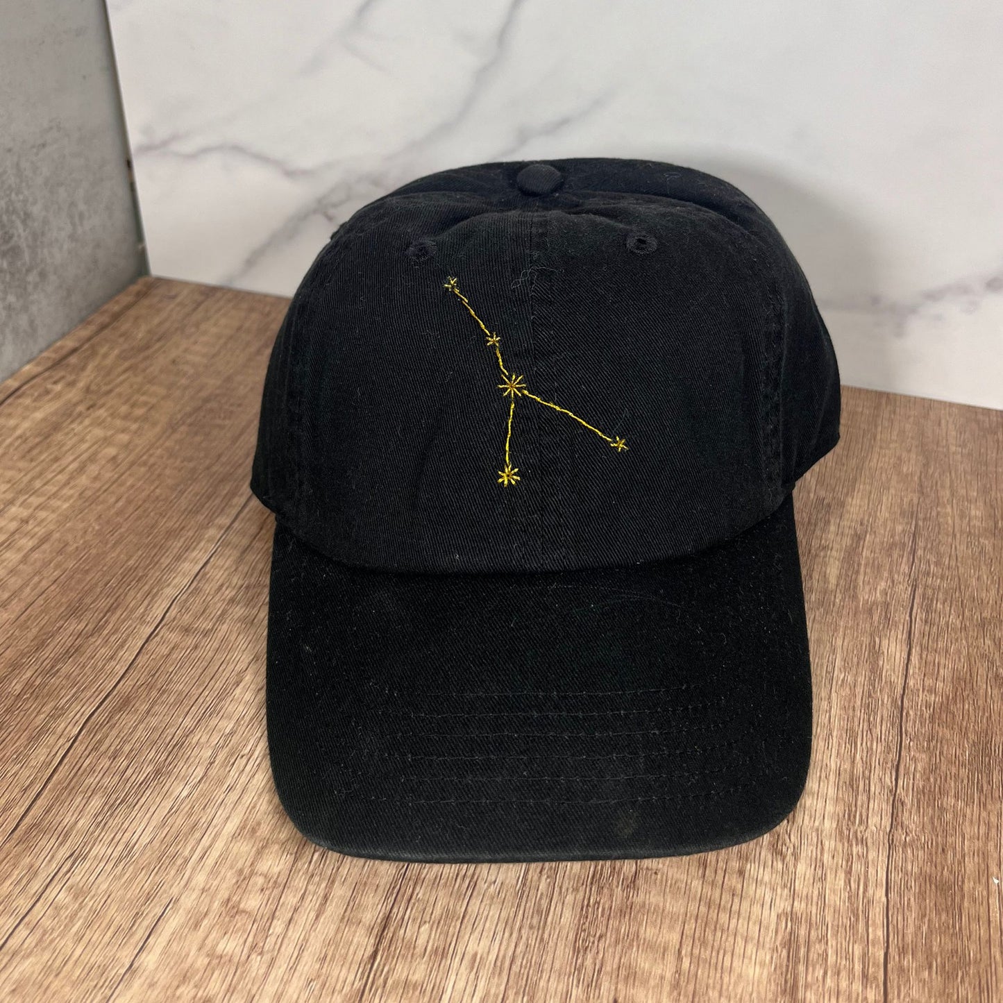 Flat-lay view of black Cancer constellation hat showcasing intricate embroidery