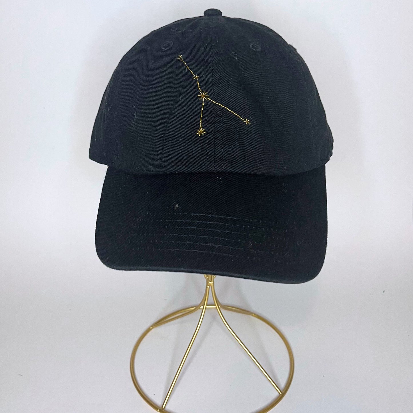 Front view of a black baseball hat with gold Cancer constellation embroidery"
