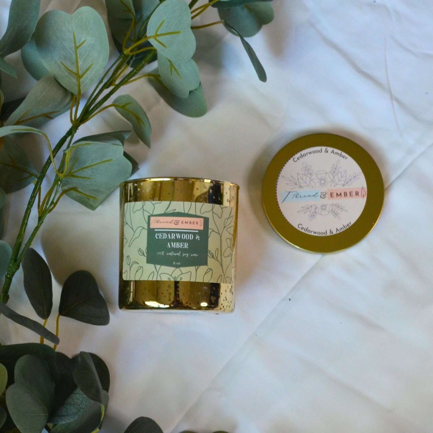 Thread & Ember candle collection featuring a variety of scented candles surrounded by fresh eucalyptus leaves.