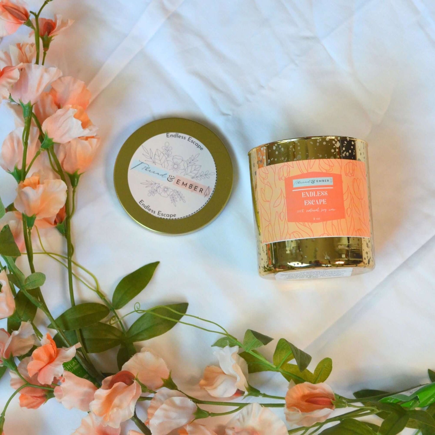 Thread & Ember Endless Escape candle in gold mercury glass with its floral-patterned lid removed, styled with soft pink flowers on a white backdrop.