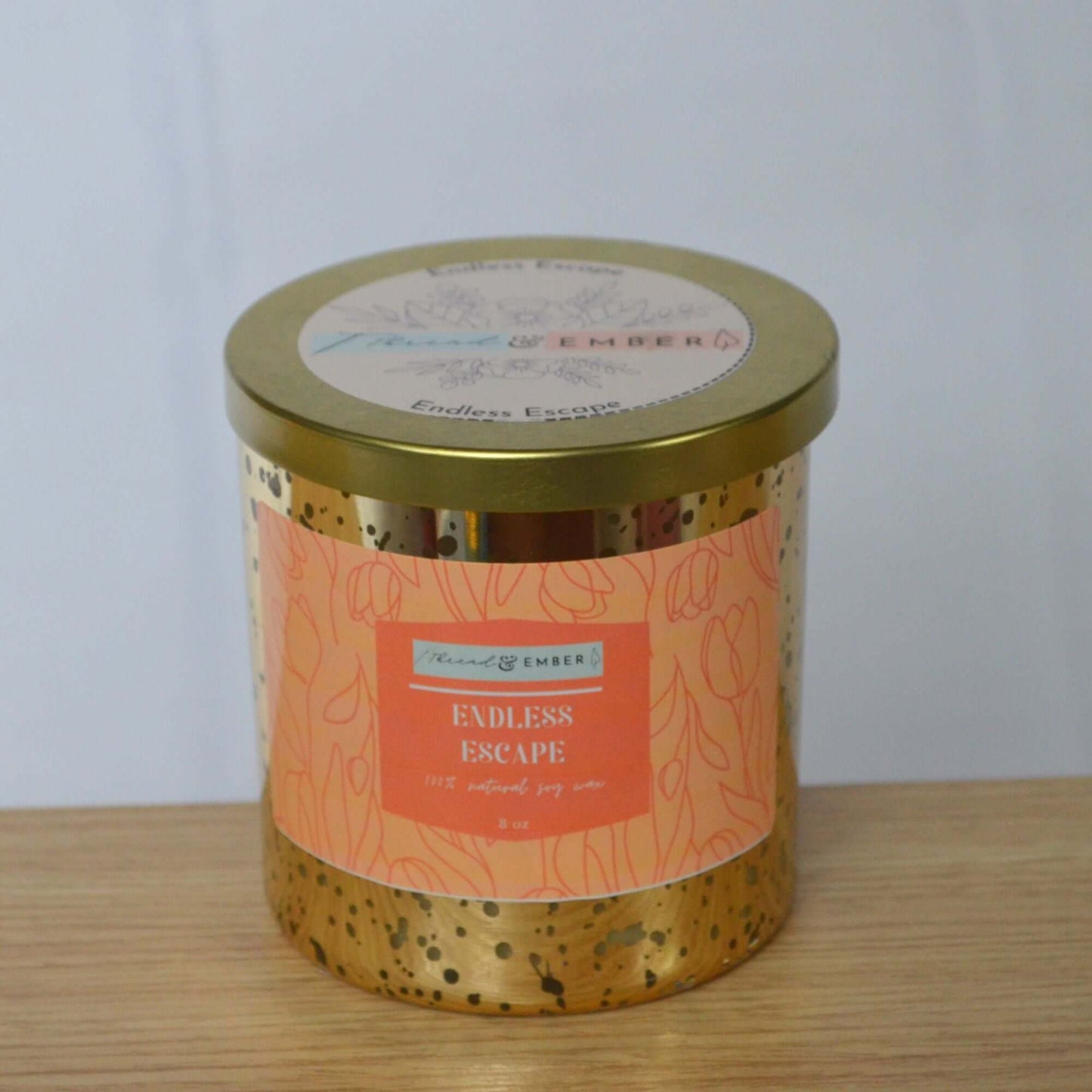 Thread & Ember Endless Escape candle in gold mercury glass with its floral-patterned lid closed, displayed on a wooden surface.