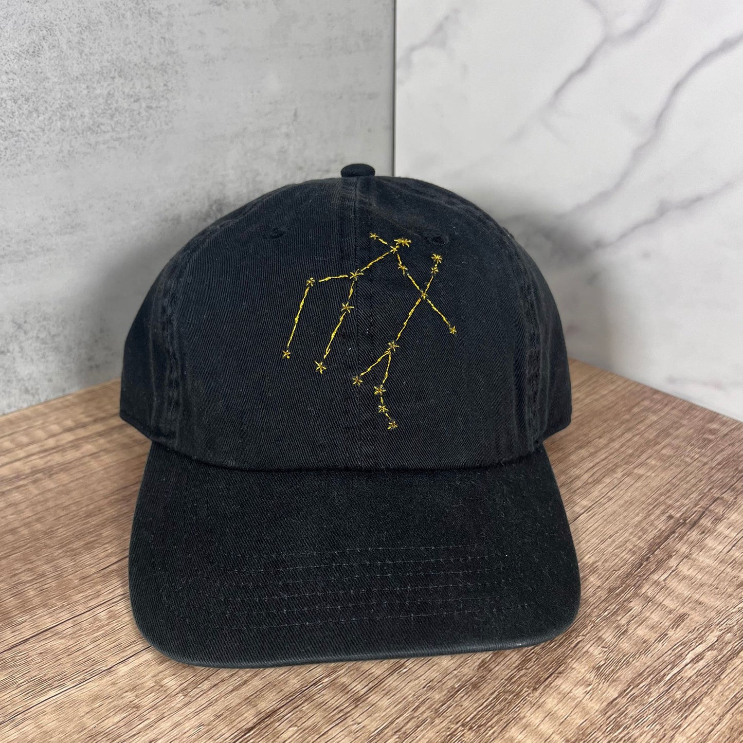 Close-up of the Gemini constellation embroidery on a black hat by Thread & Ember.