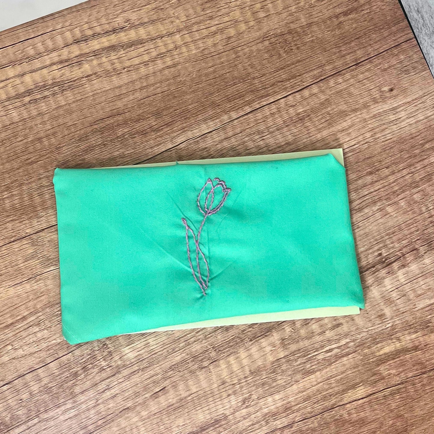 Green pet bandana with pink tulip embroidery, folded and displayed on a natural wooden surface.
