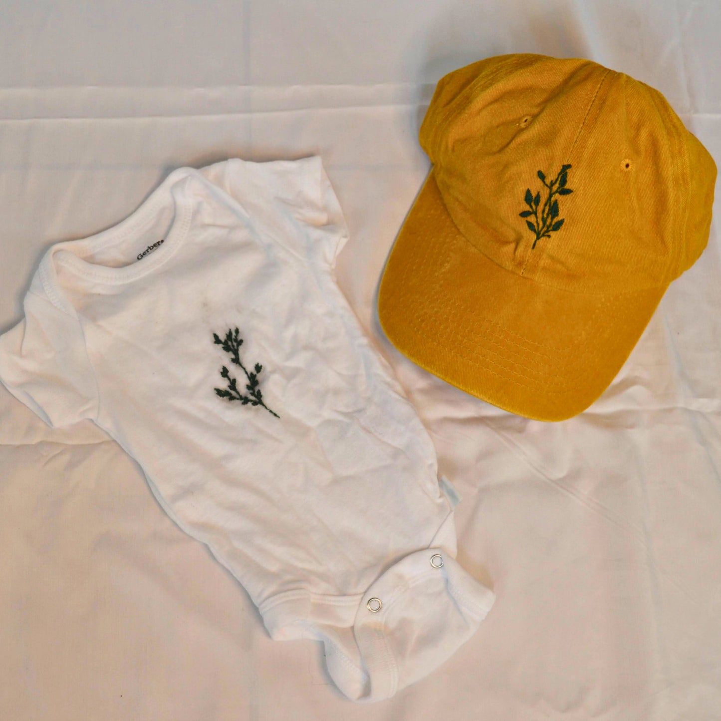 Greenery embroidered baby onesie styled with a mustard baseball hat for inspiration (hat not included).
