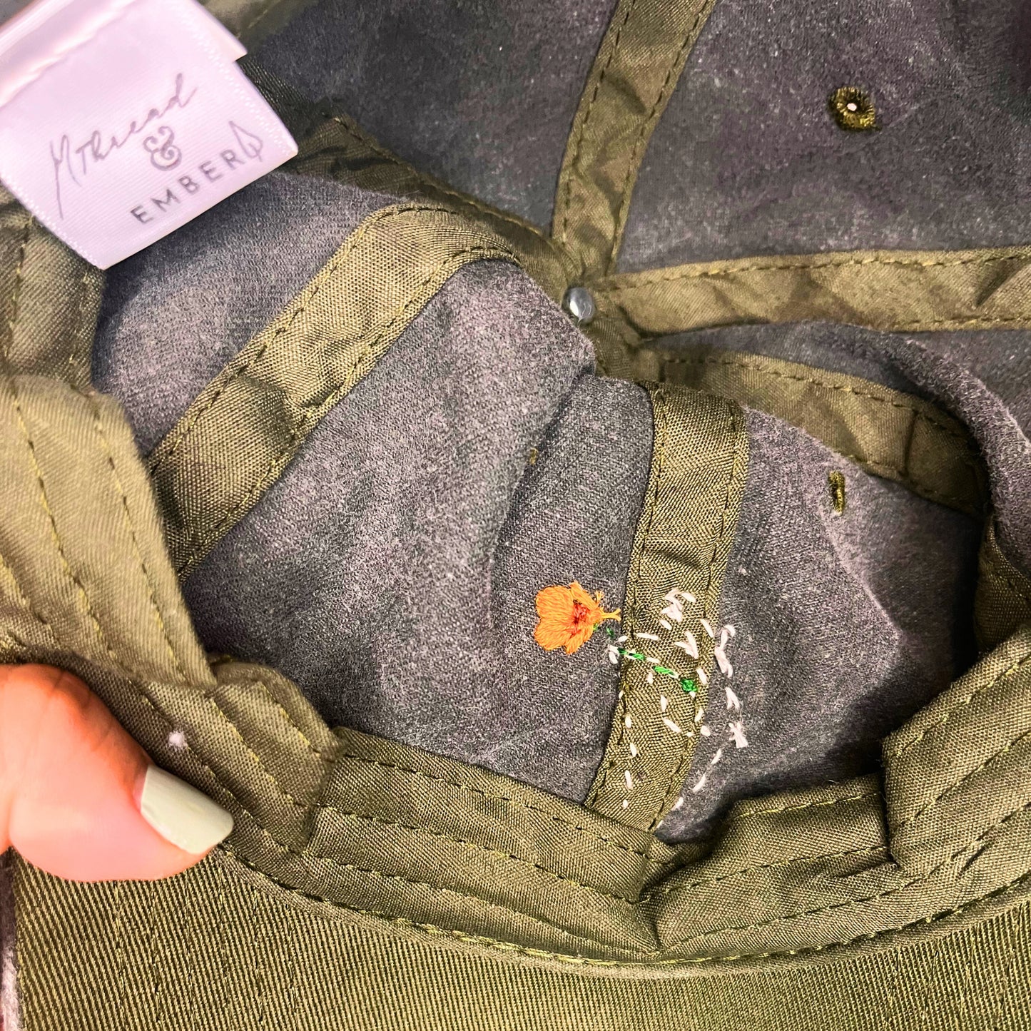 Interior of a green baseball cap showing detailed stitching and a golden poppy design inside the brim.