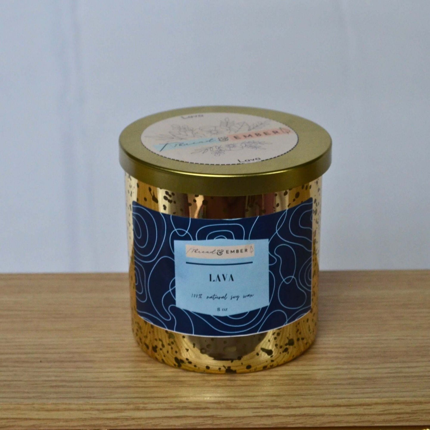 Thread & Ember Lava candle with luxurious gold speckled holder and bold blue label on a wooden table, featuring a clean and minimalist aesthetic.