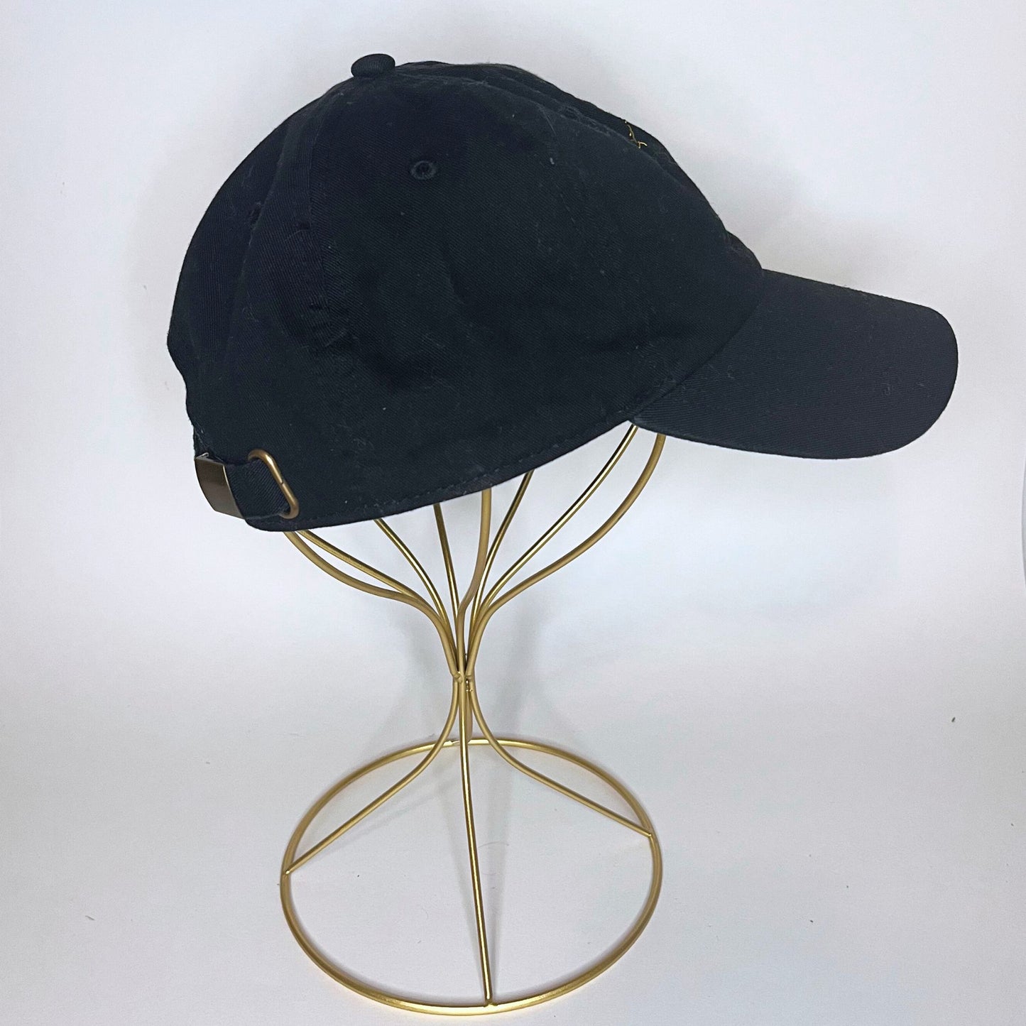 Alternate side view of a black cap with a golden Libra constellation embroidery, presented on a minimalist gold wire stand.