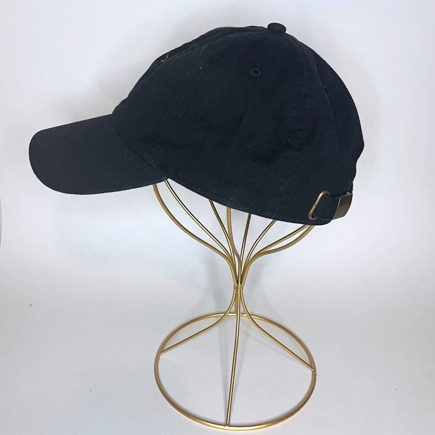 Side view of a black cap featuring the Libra constellation embroidered in golden thread, displayed on a gold wire stand.