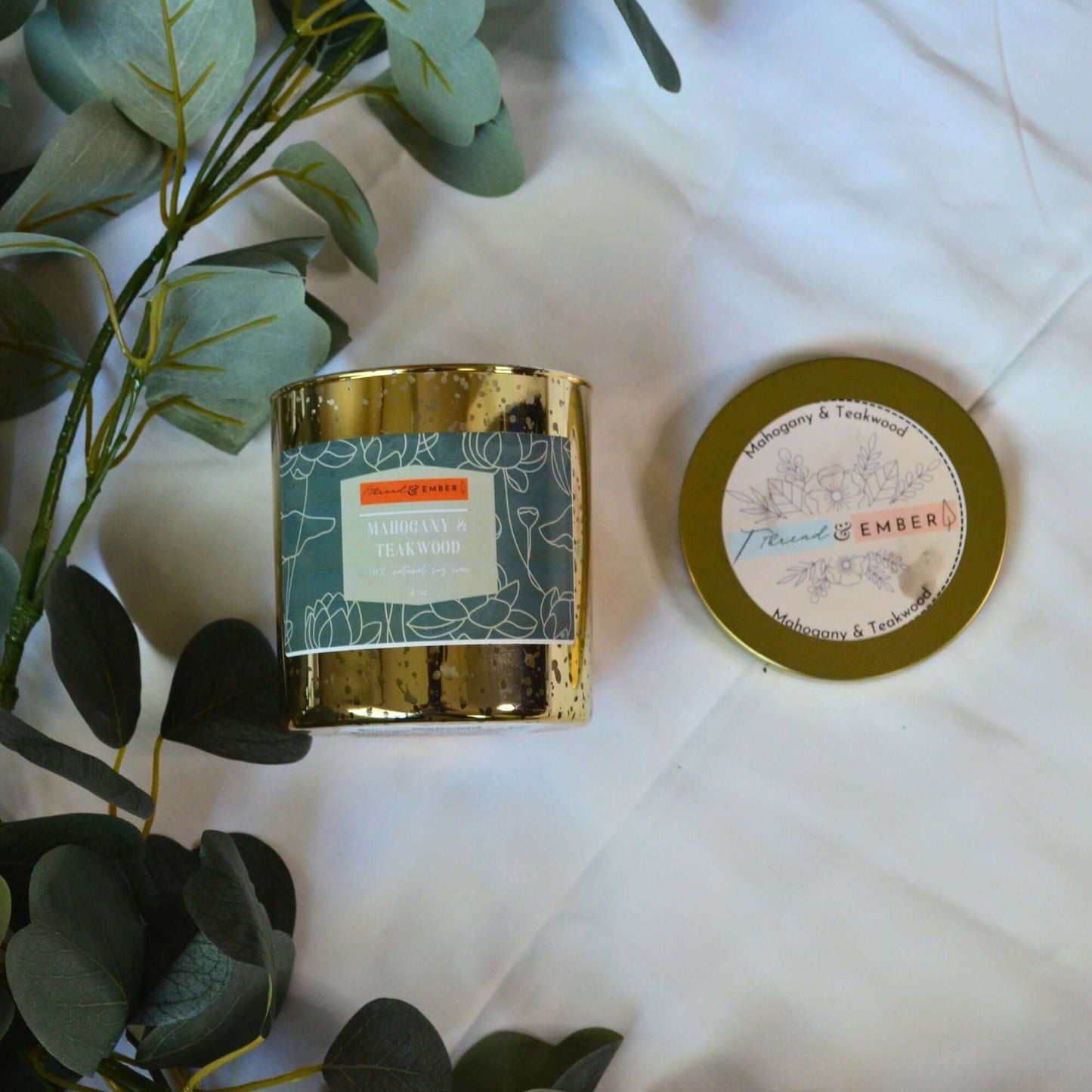 Overhead view of the Mahogany & Teakwood Candle with its elegant lid, surrounded by eucalyptus leaves.