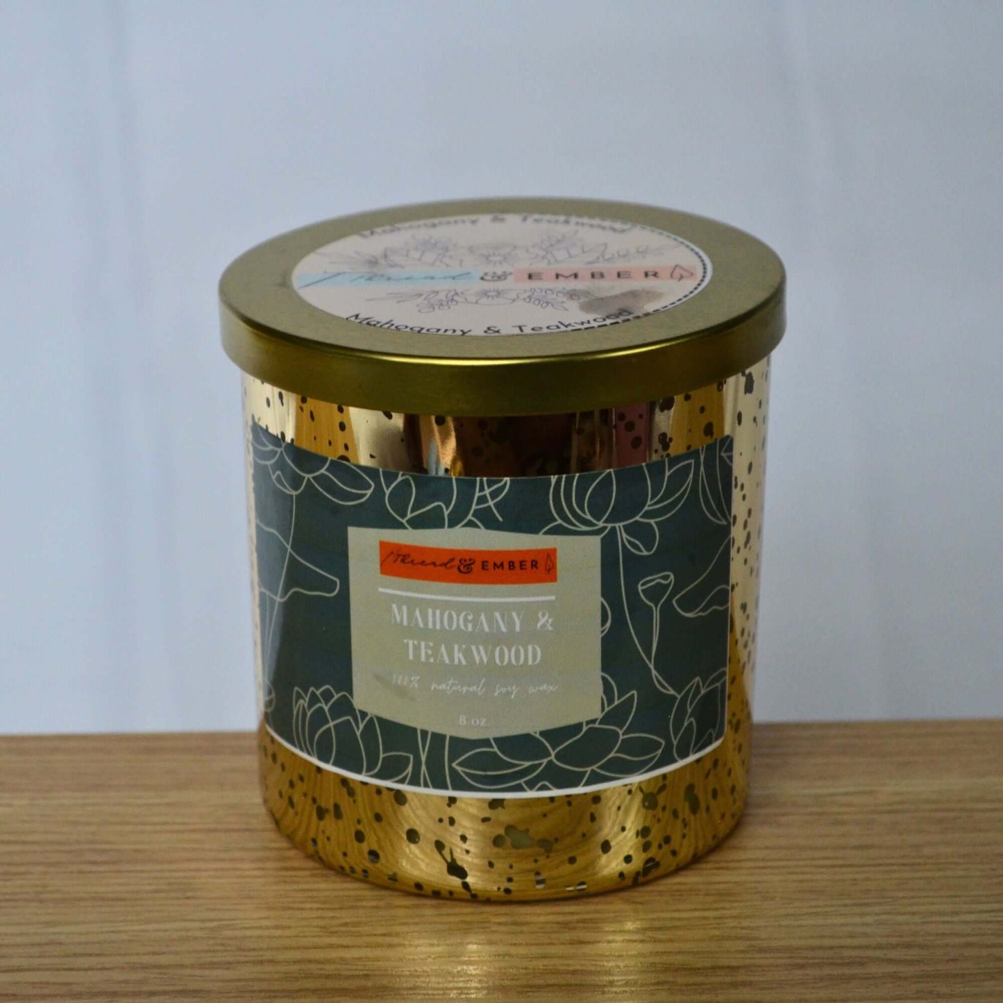 Close-up of the Mahogany & Teakwood Candle in a gold mercury glass container on a wooden surface.