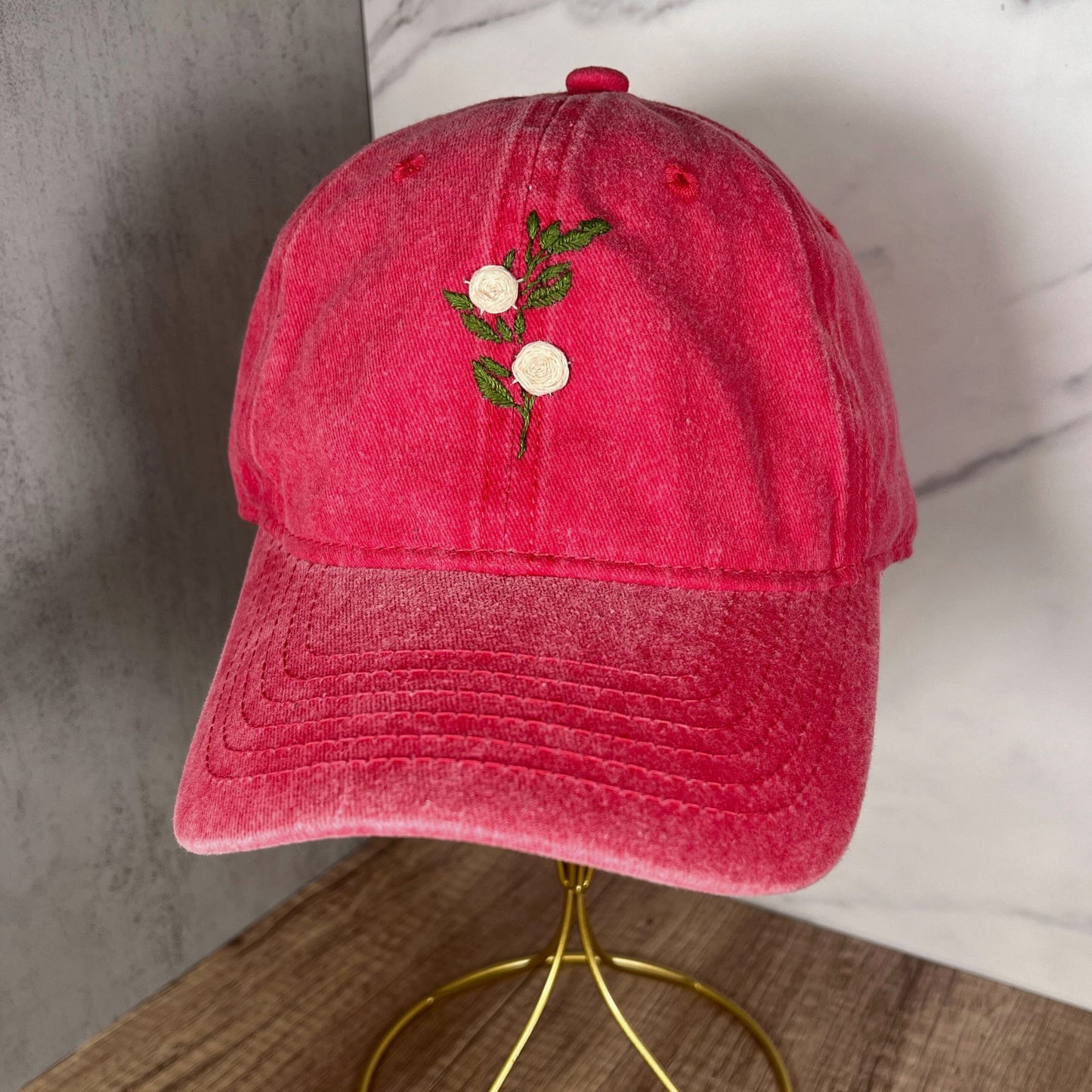 Front view of a red distressed dad hat featuring two embroidered white roses with green leaves on the front panel.
