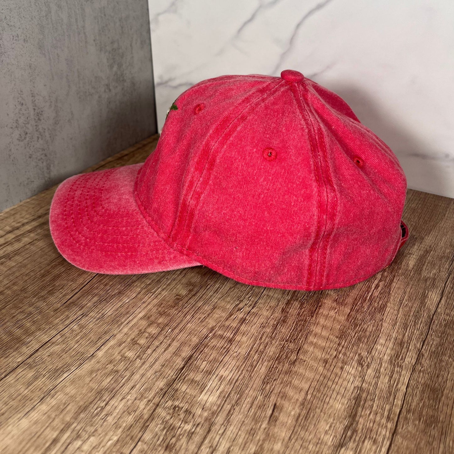 Side view of a red dad hat featuring a subtle curve of the brim and the embroidered white roses design visible on the side.