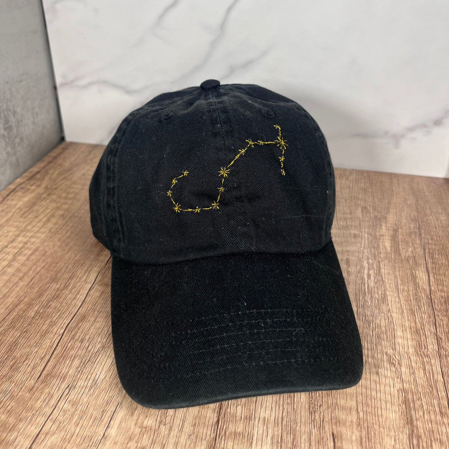 Black Scorpio zodiac constellation embroidered hat shown from the front on a wooden surface.