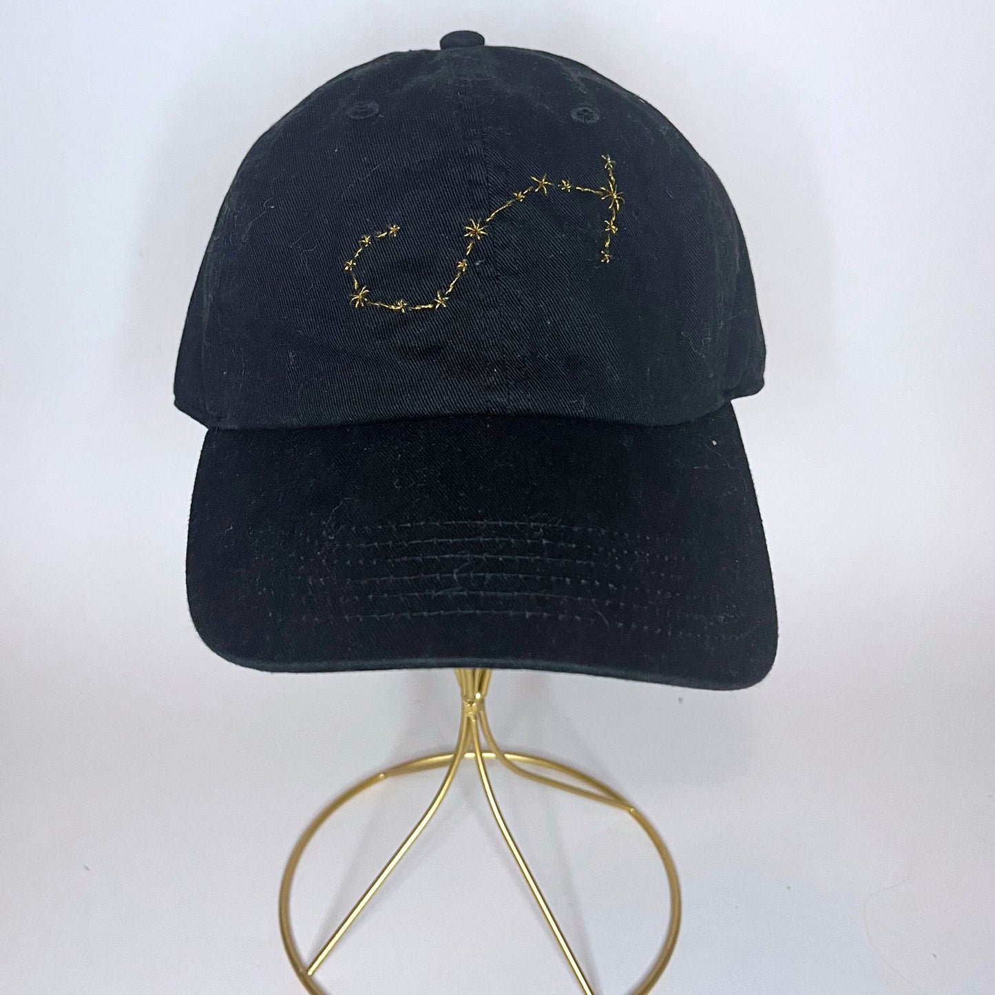 Front view of a Scorpio constellation hat featuring gold embroidery of the zodiac symbol.
