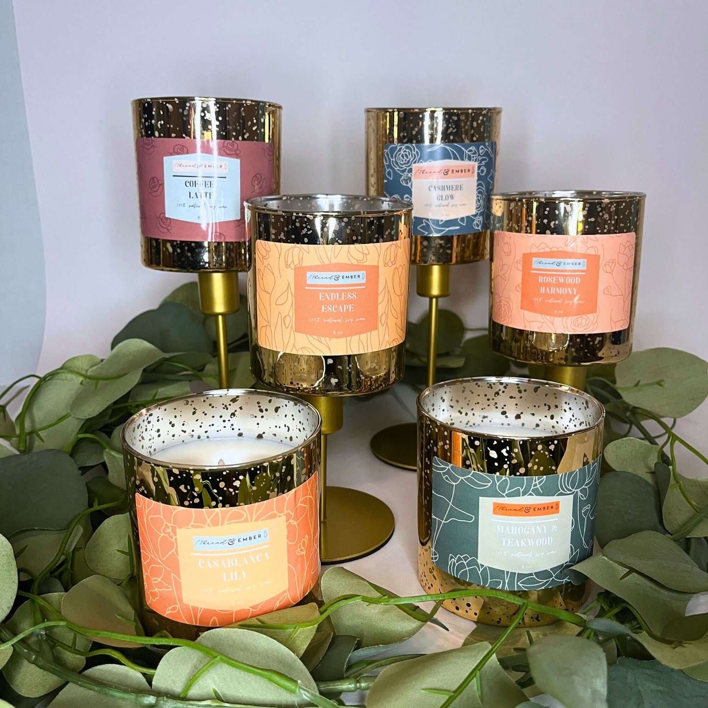 Collection of luxury scented candles from Thread & Ember, featuring elegant gold mercury jars and natural soy wax, displayed with green eucalyptus decor."