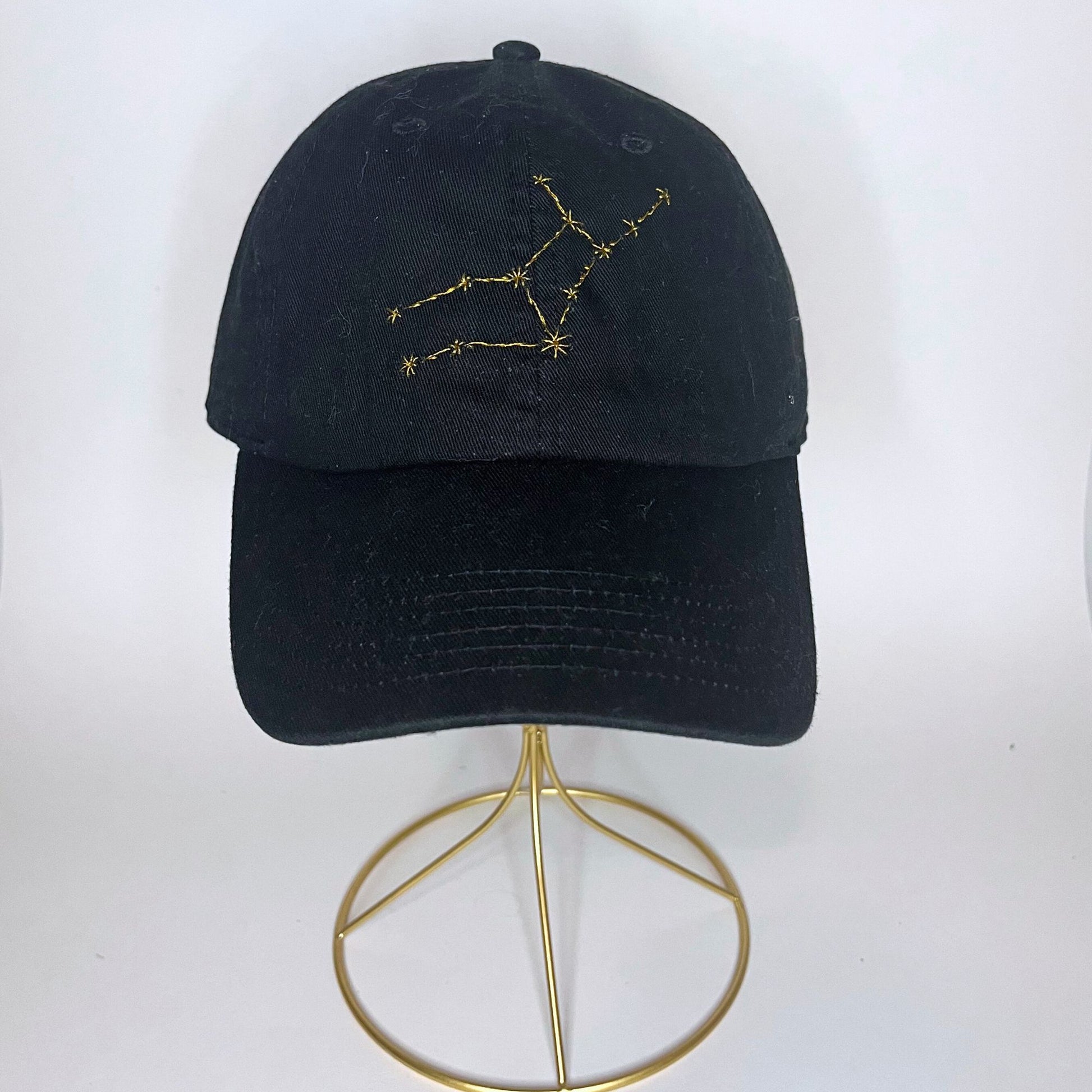 Black cap with embroidered Virgo constellation design in golden thread, displayed on a wooden surface.