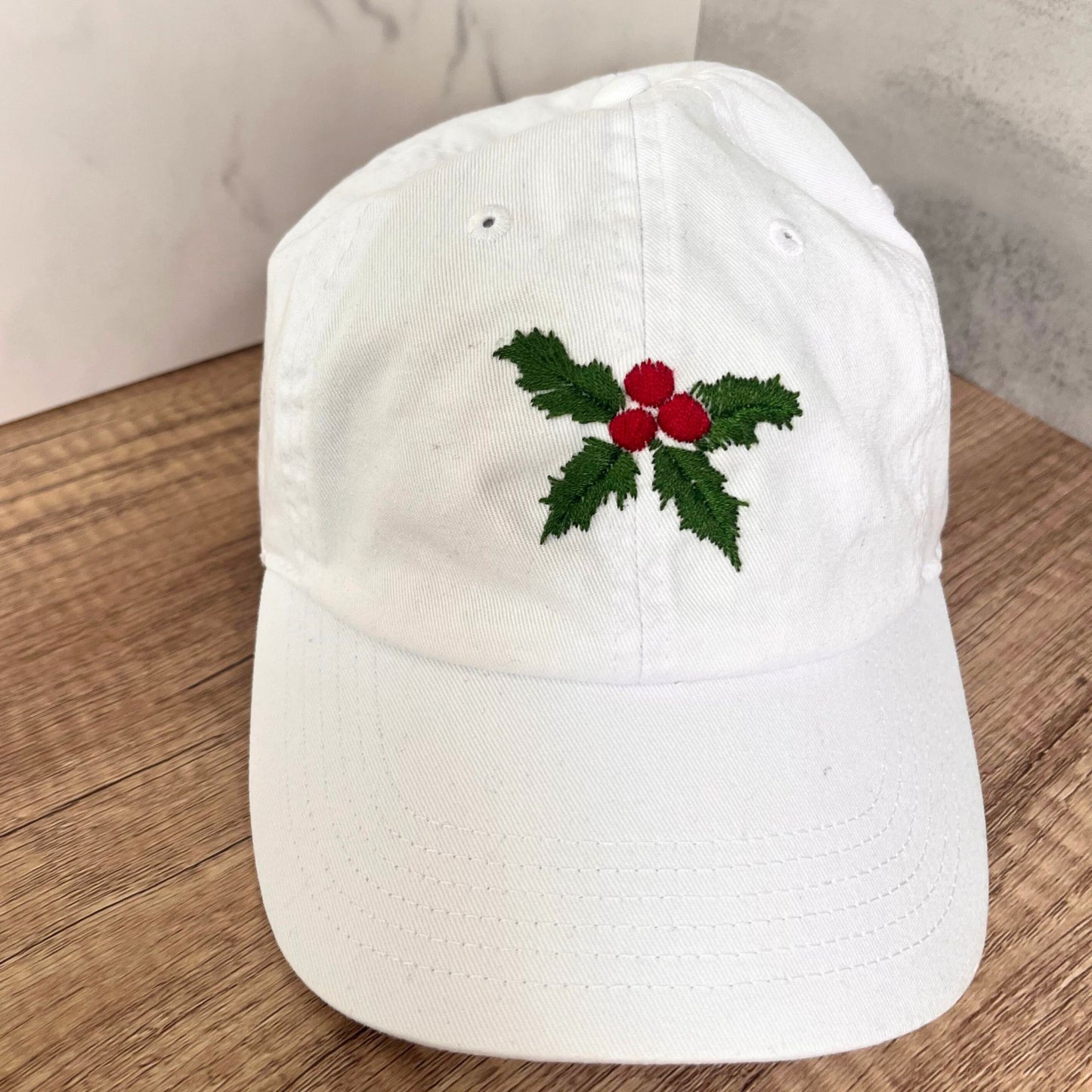 Front view of a white hat featuring vibrant holly and berry embroidery.