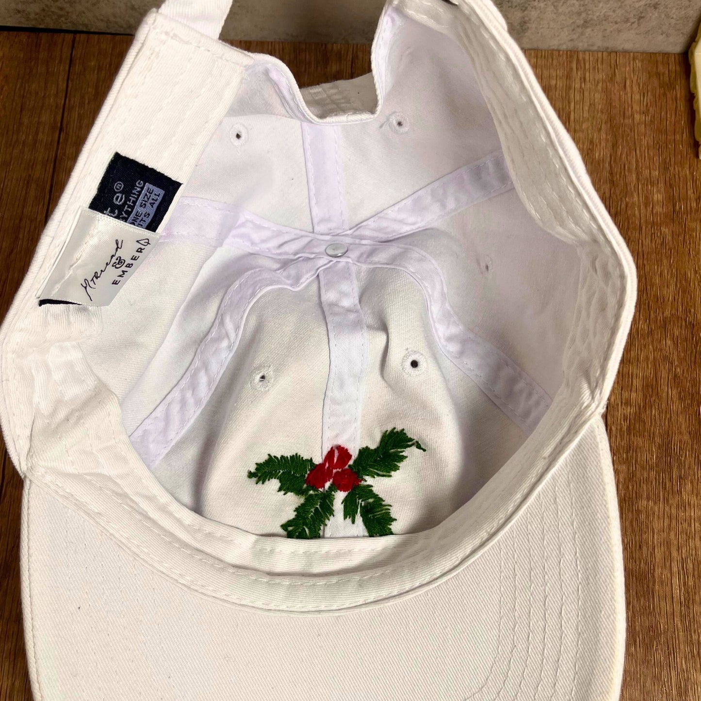 Overhead view of a white hat with hand-embroidered holly and berries for a detailed look.