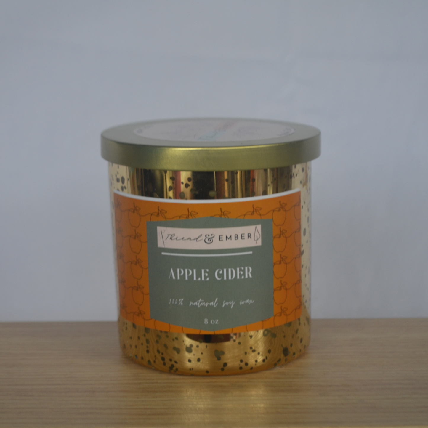 Thread & Ember Apple Cider Candle in an elegant gold jar, standing against a neutral background.