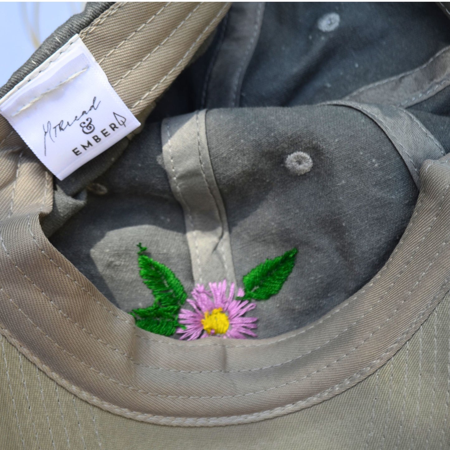 Close-up of the inside embroidery of a grey baseball hat with gerber daisies by Thread & Ember.