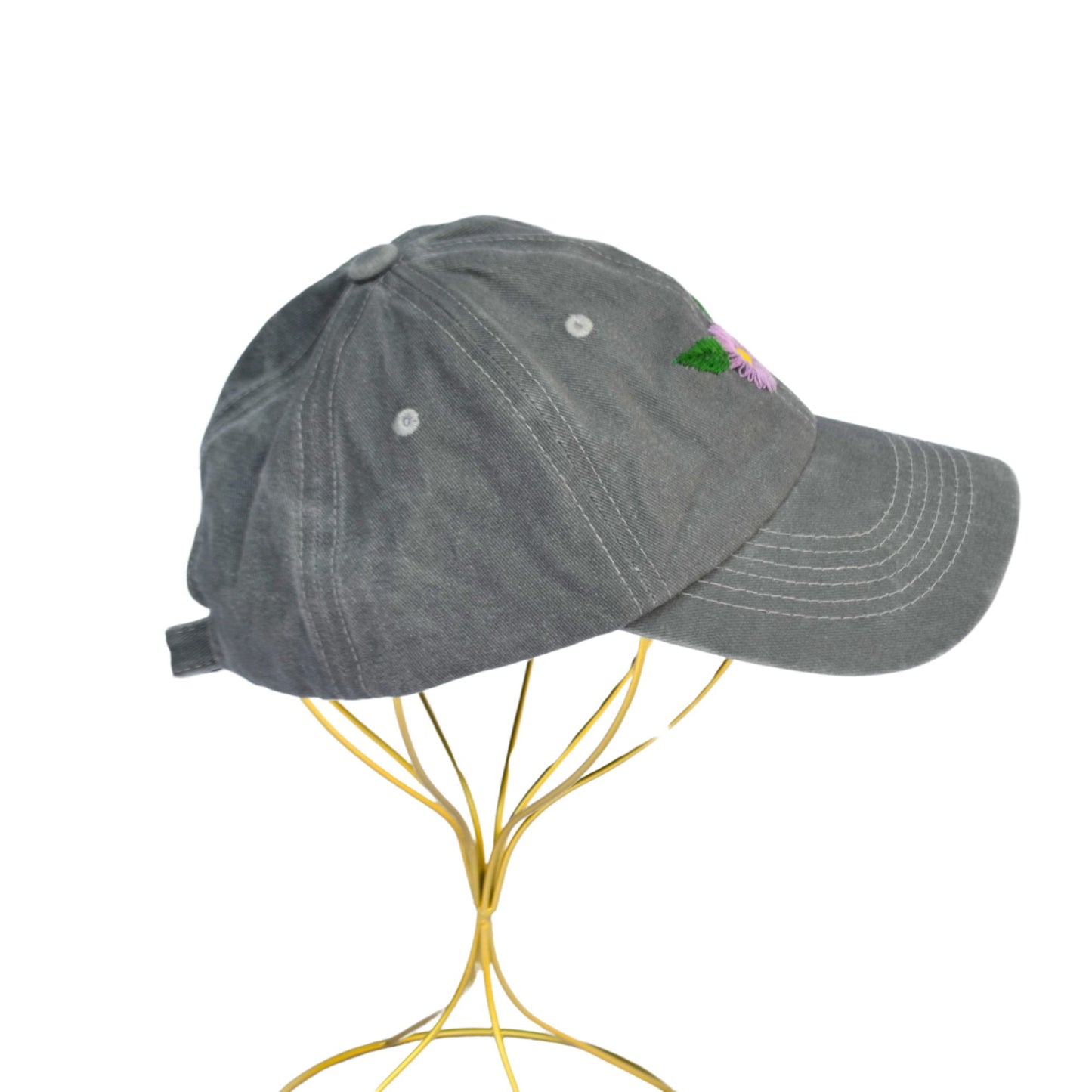 Side angle of a grey baseball cap featuring floral embroidery of gerber daisies.