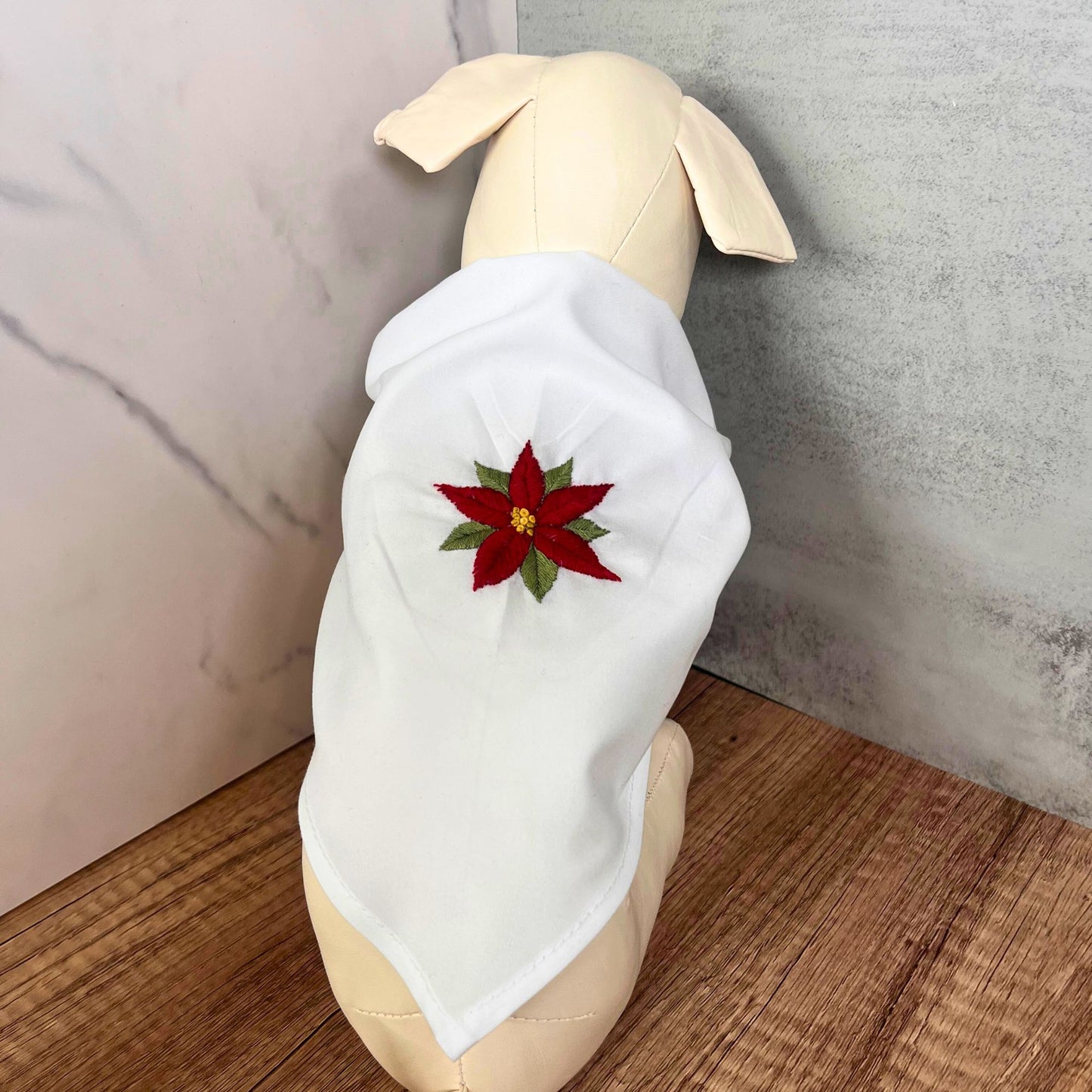 White cotton pet bandana with hand-embroidered red poinsettia design, modeled on a dog, highlighting the festive embroidery.