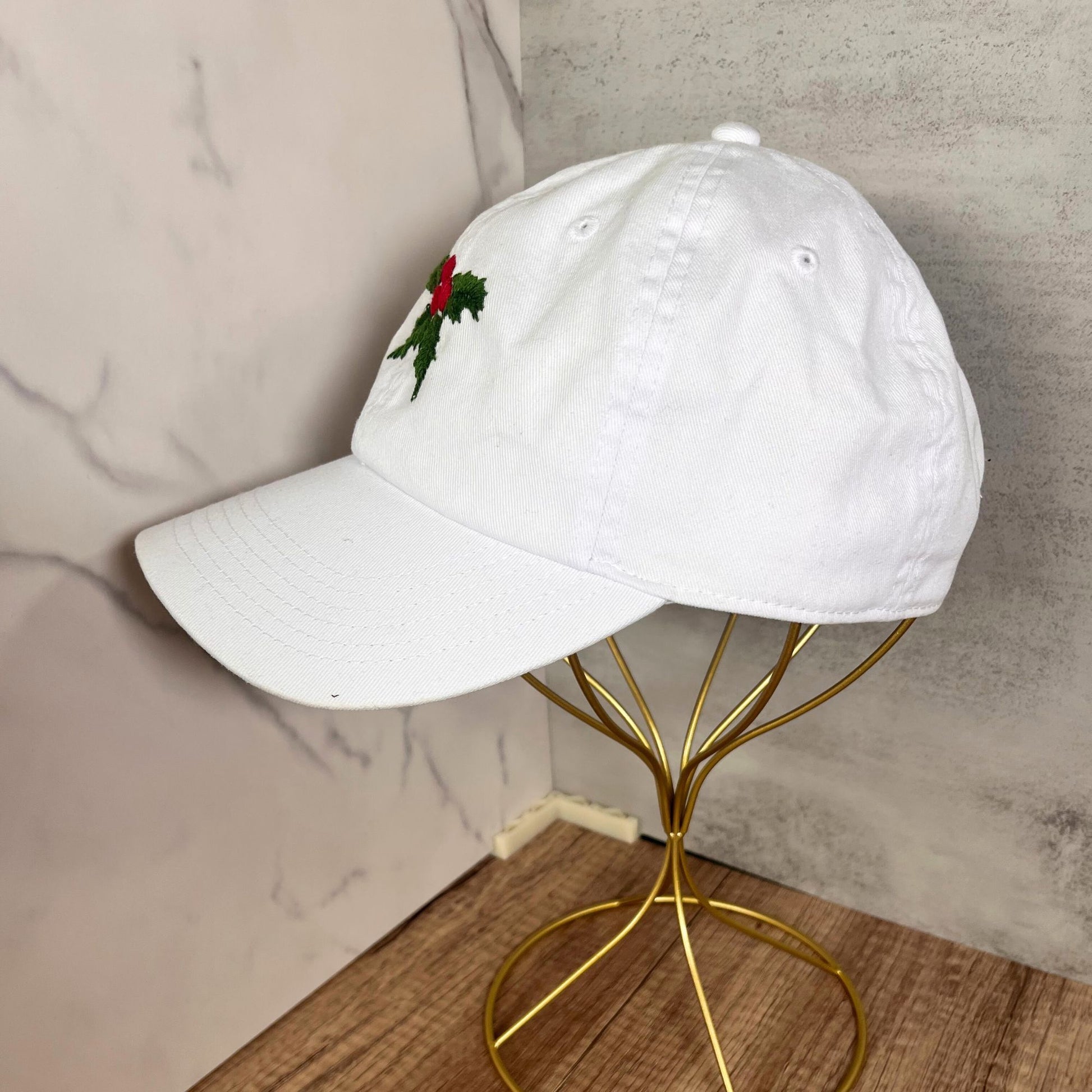 White hat with holly and berry embroidery, side view on a golden hat stand.